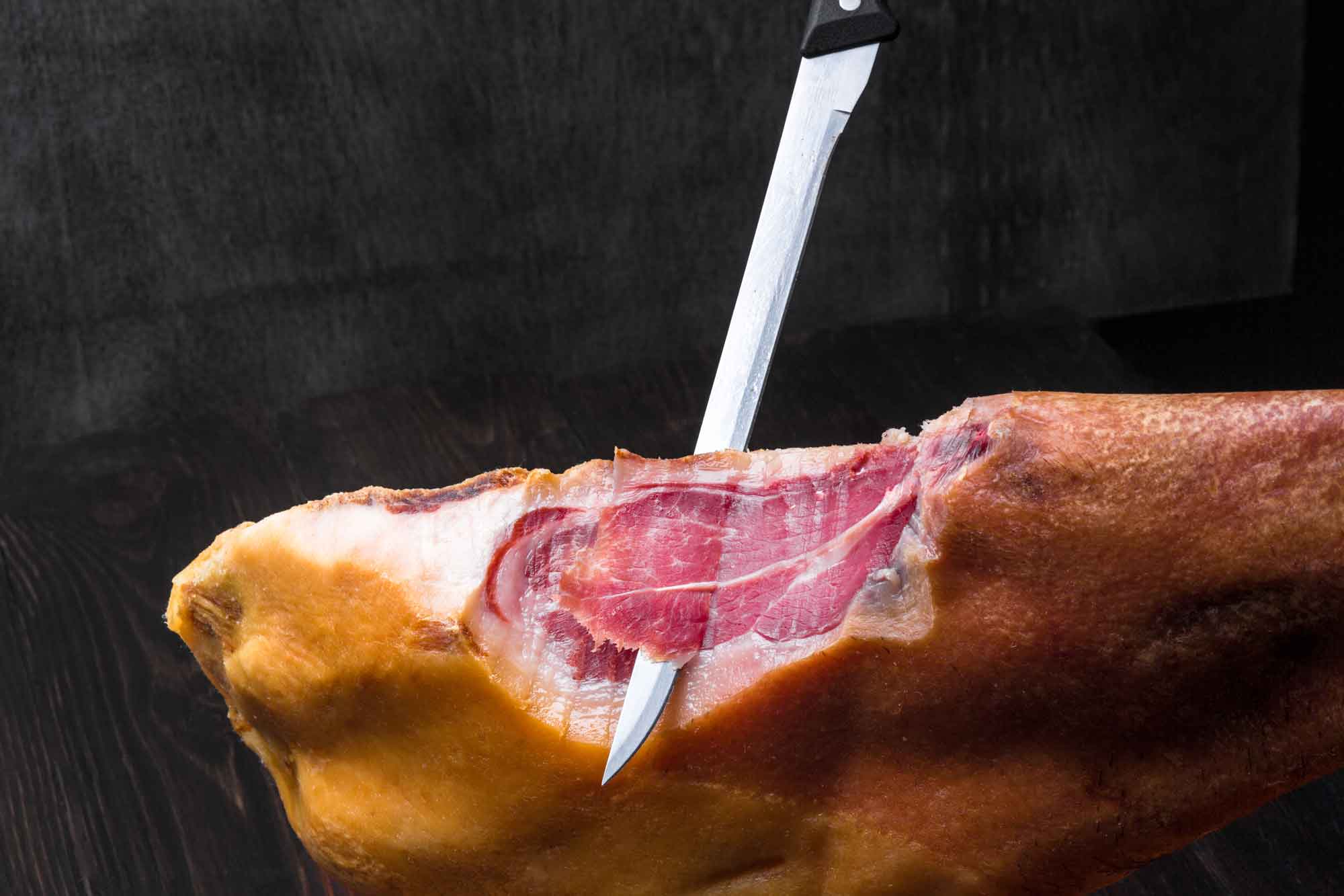 cuchillo jamonero cortando una loncha de jamón iberico sobre fondo negro 